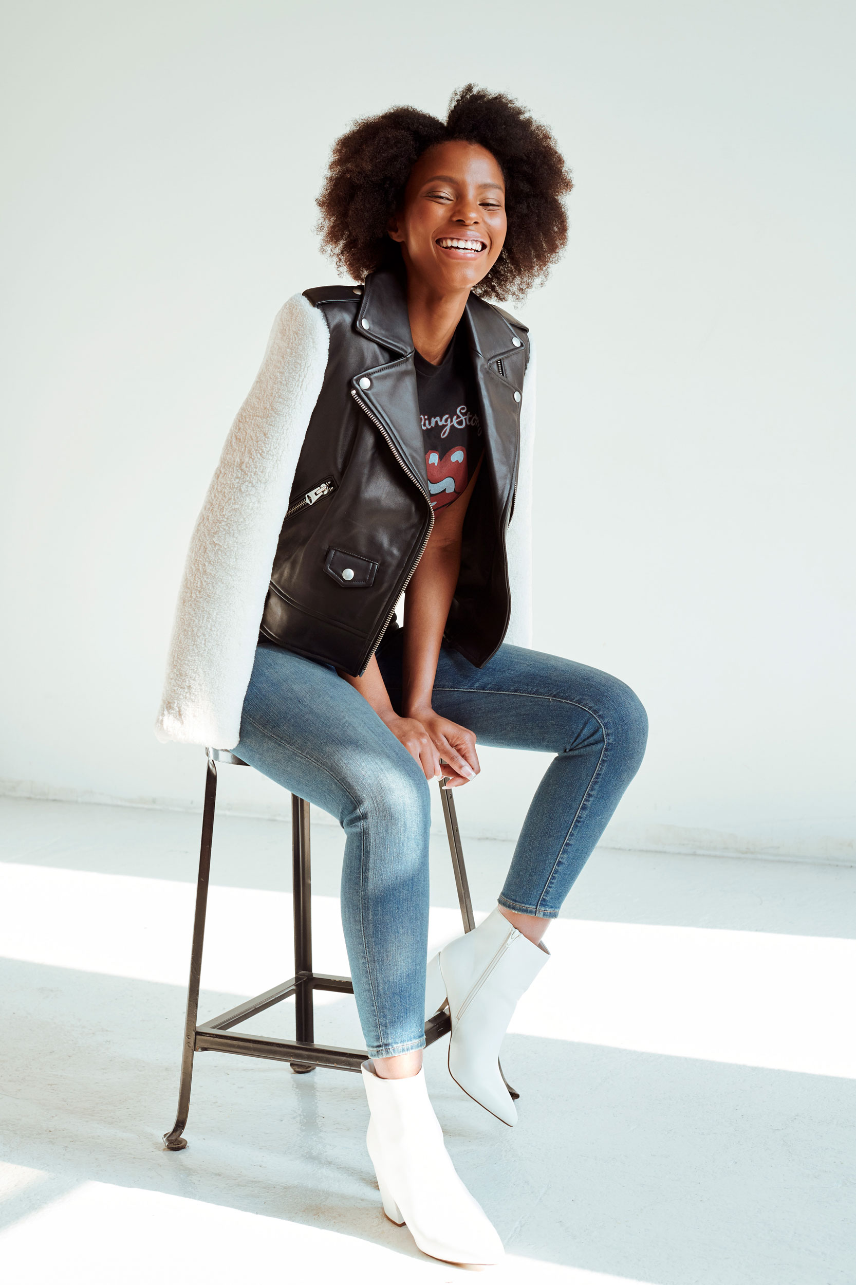 Laughing female styled in Rolling Stones tee, leather jacket, jeans and white ankle boots