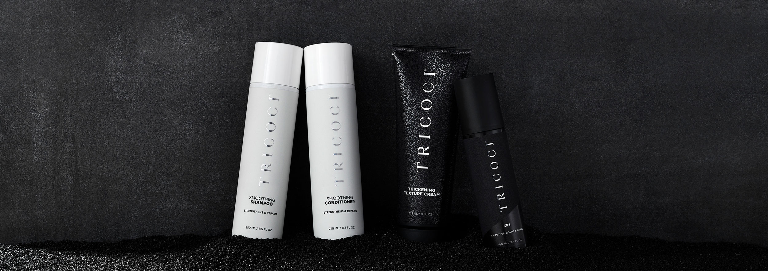 Four black and white haircare products nestled in black sand
