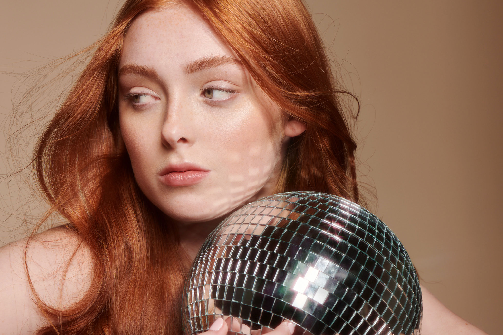 Portrait of female model holding a disco ball featuring a clean, no-makeup look and soft curls