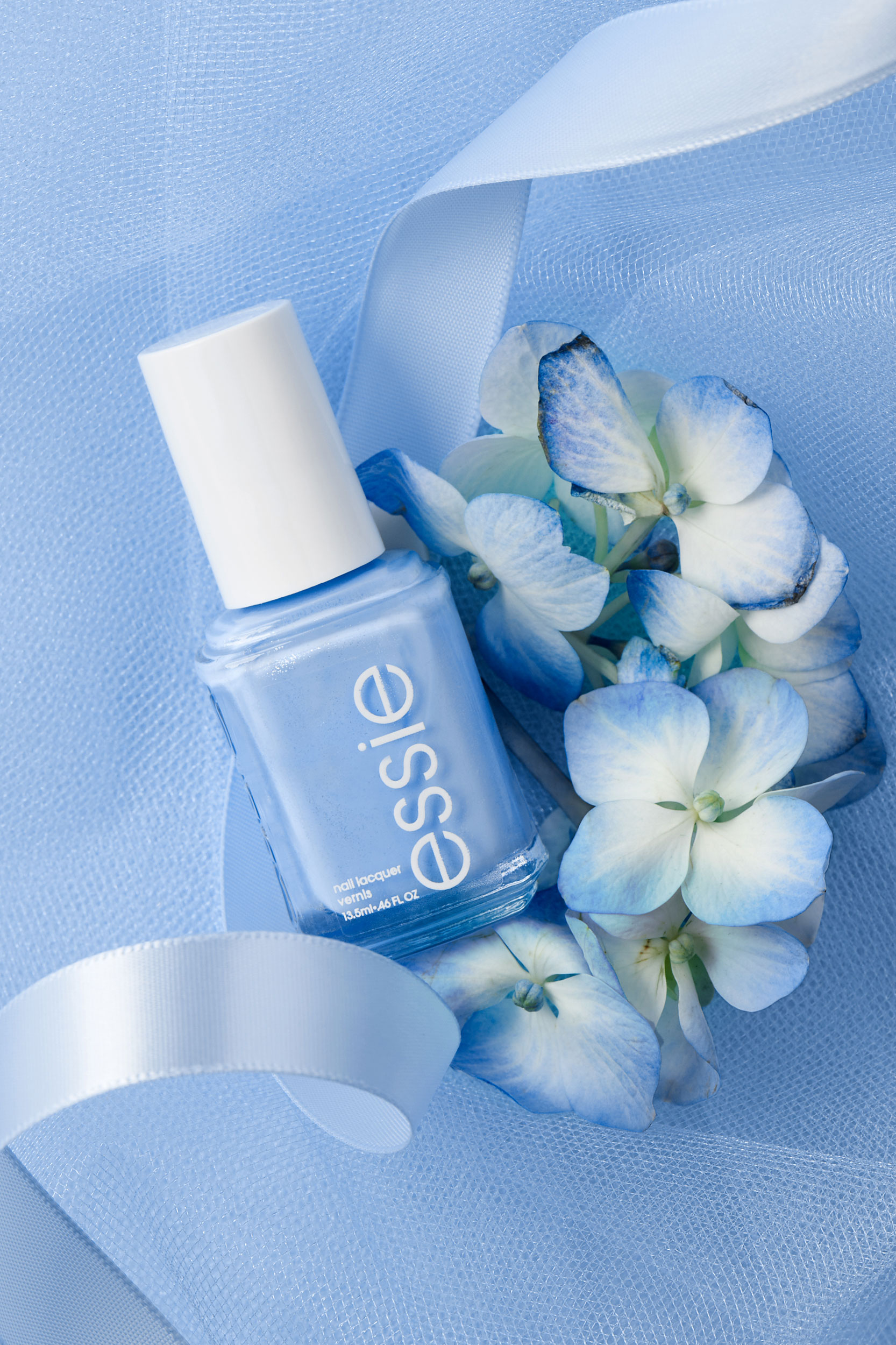 Cornflower blue nail polish bottle nestled in tulle, ribbon and flowers