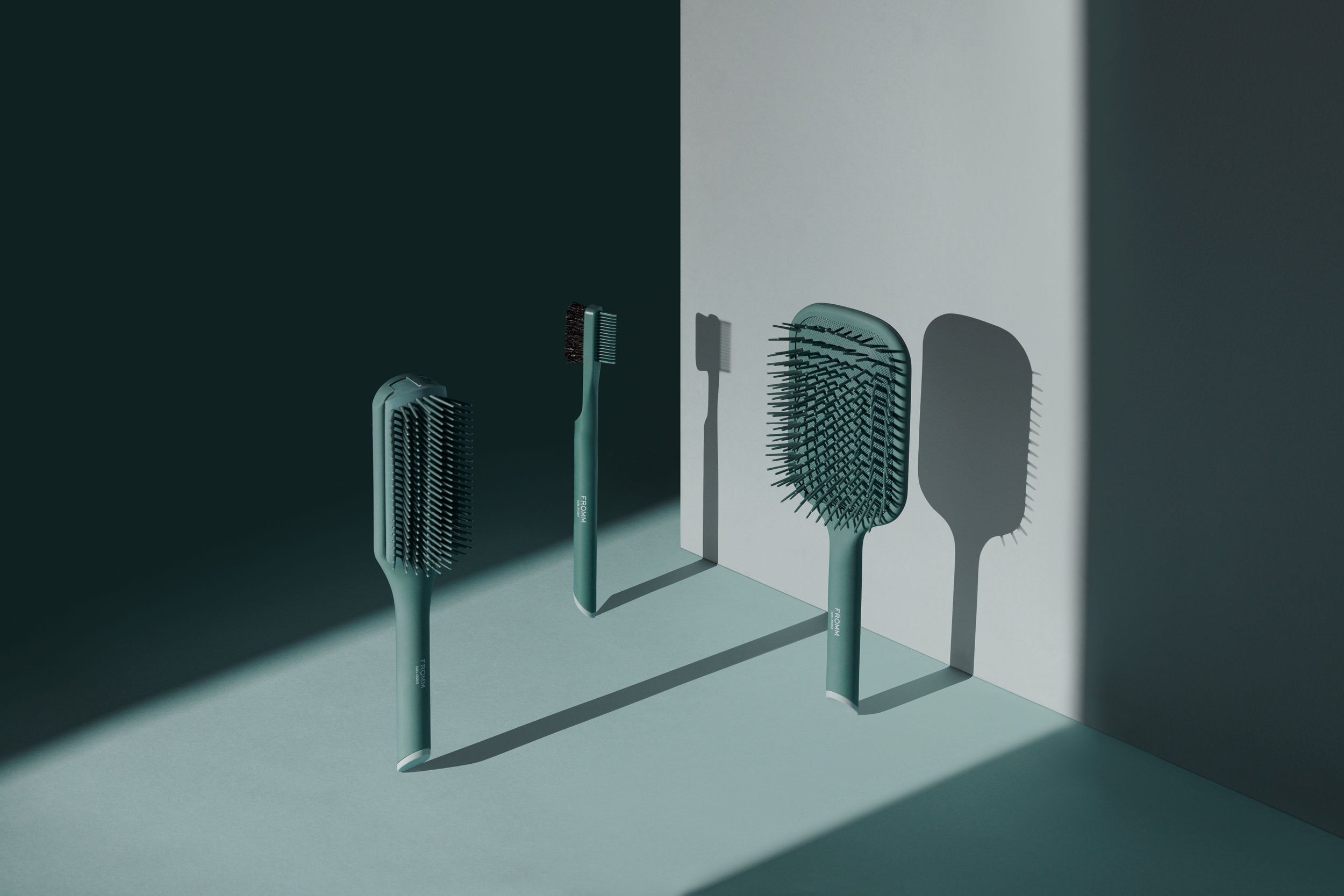 Pair of green brushes with edge shaper brush/comb suspended vertically and lit to cast a long shadow