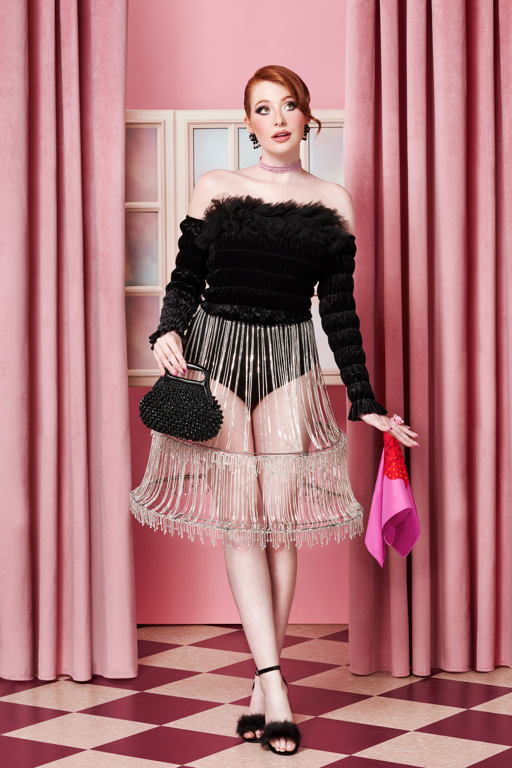 Red-haired model styled in black, ruffled bodysuit and chandelier-style hoop skirt with purse and scarf inspired by Barbie