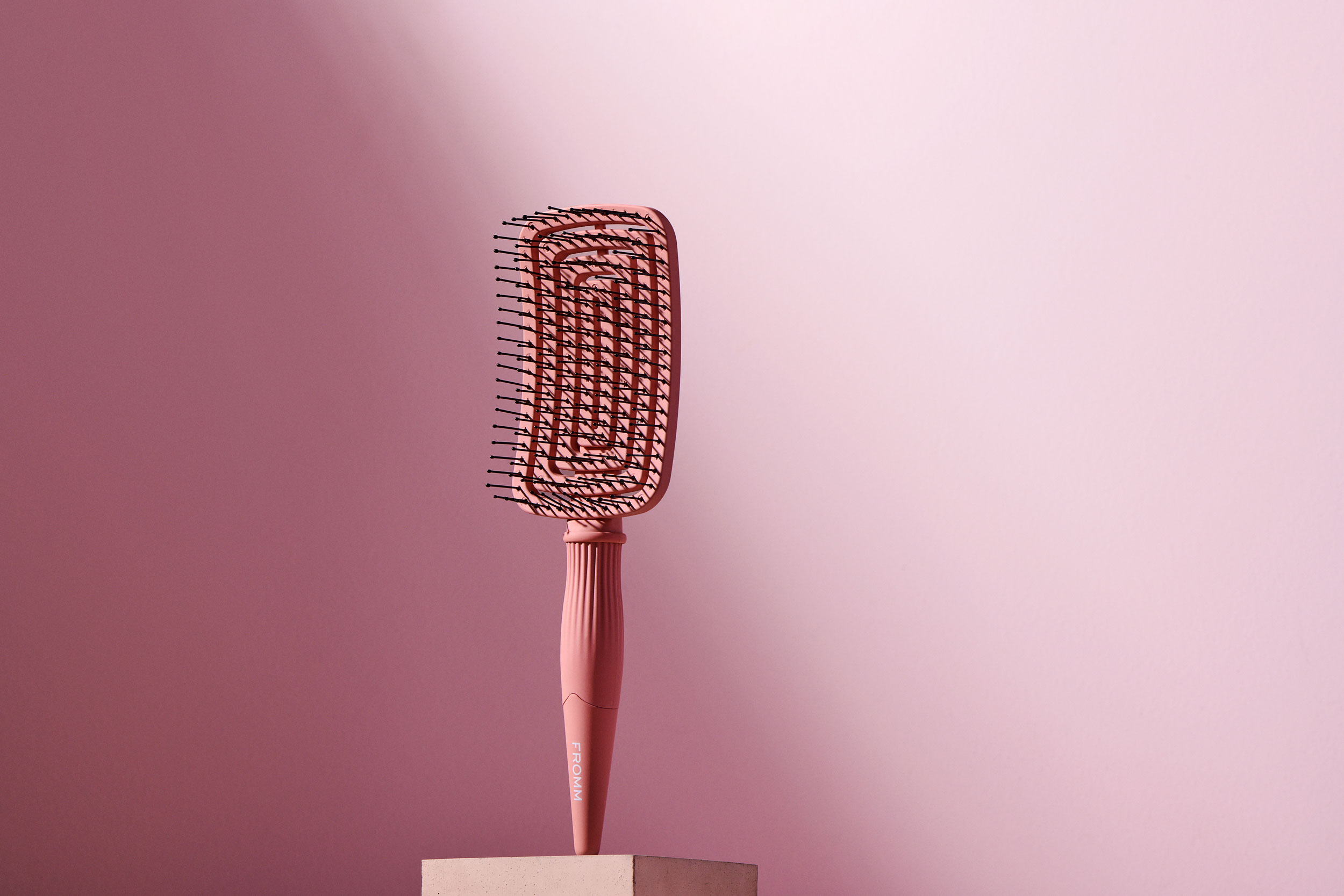 Pink detangling vent brush suspended vertically on pedestal 