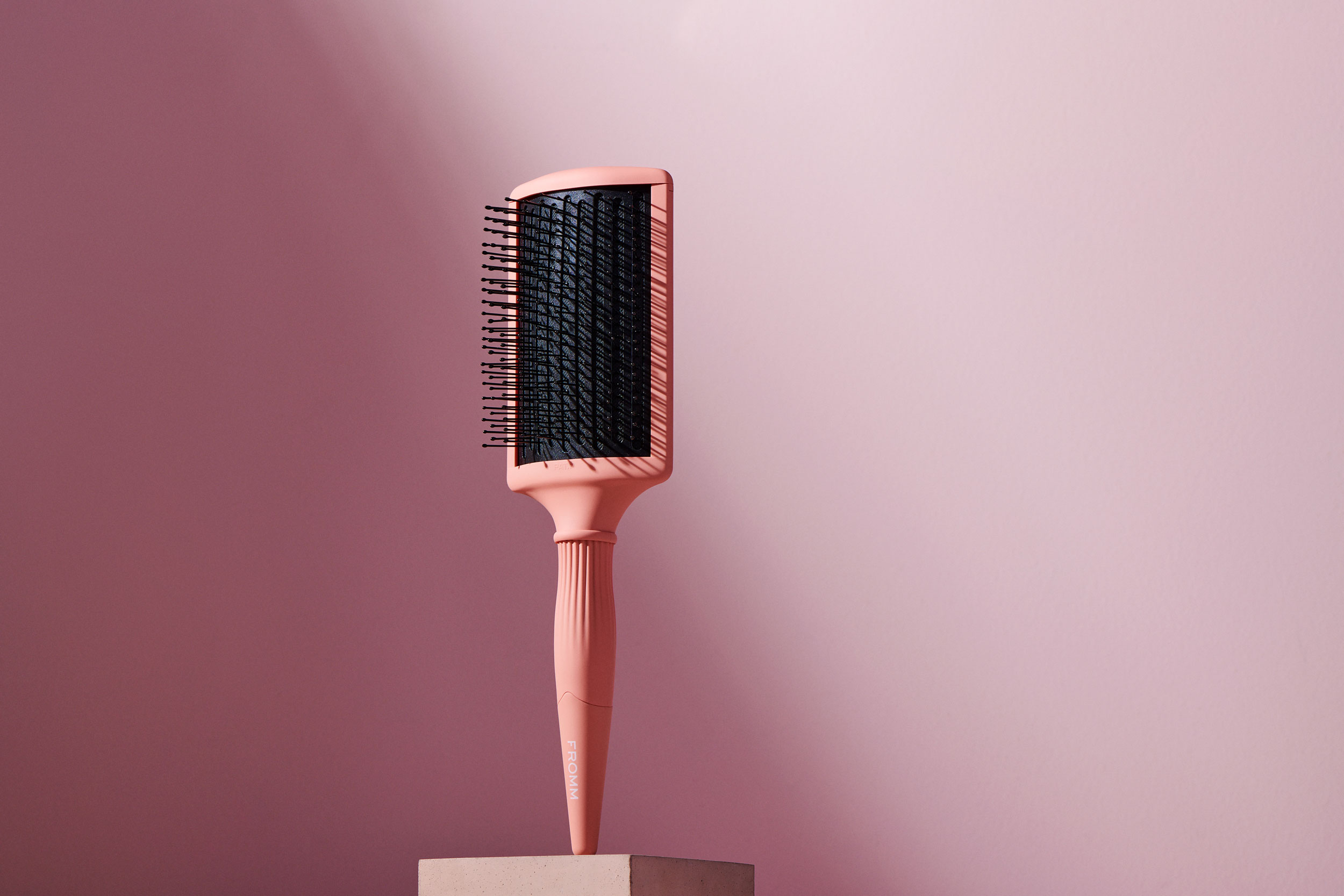 Pink paddle brush suspended on pedestal