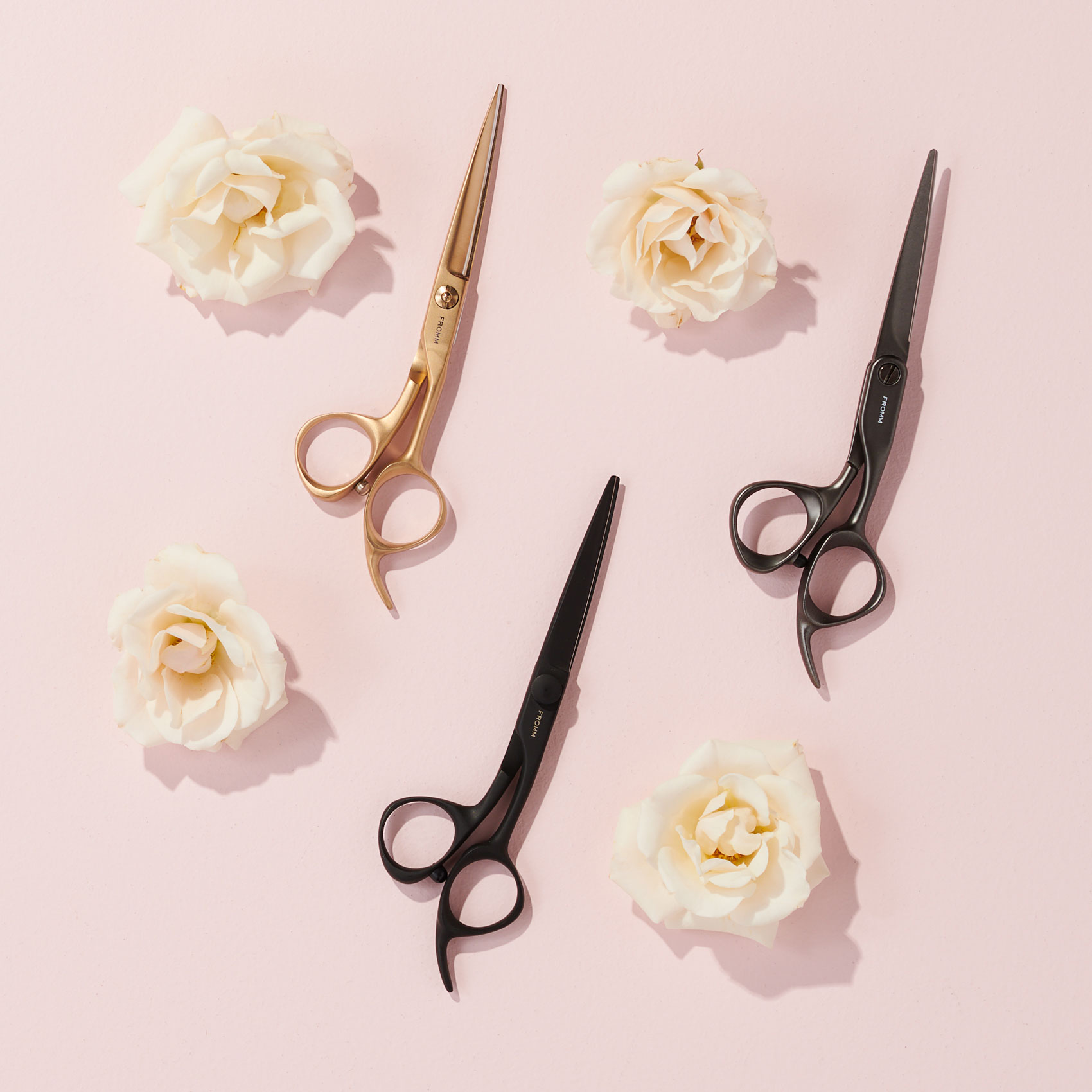 Three hair cutting shears on pale pink surface with white roses