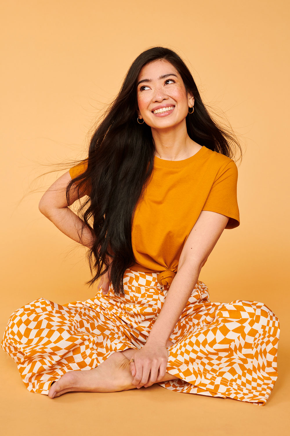 Barefoot female model styled in playfully patterned orange and white pants with matching orange tee
