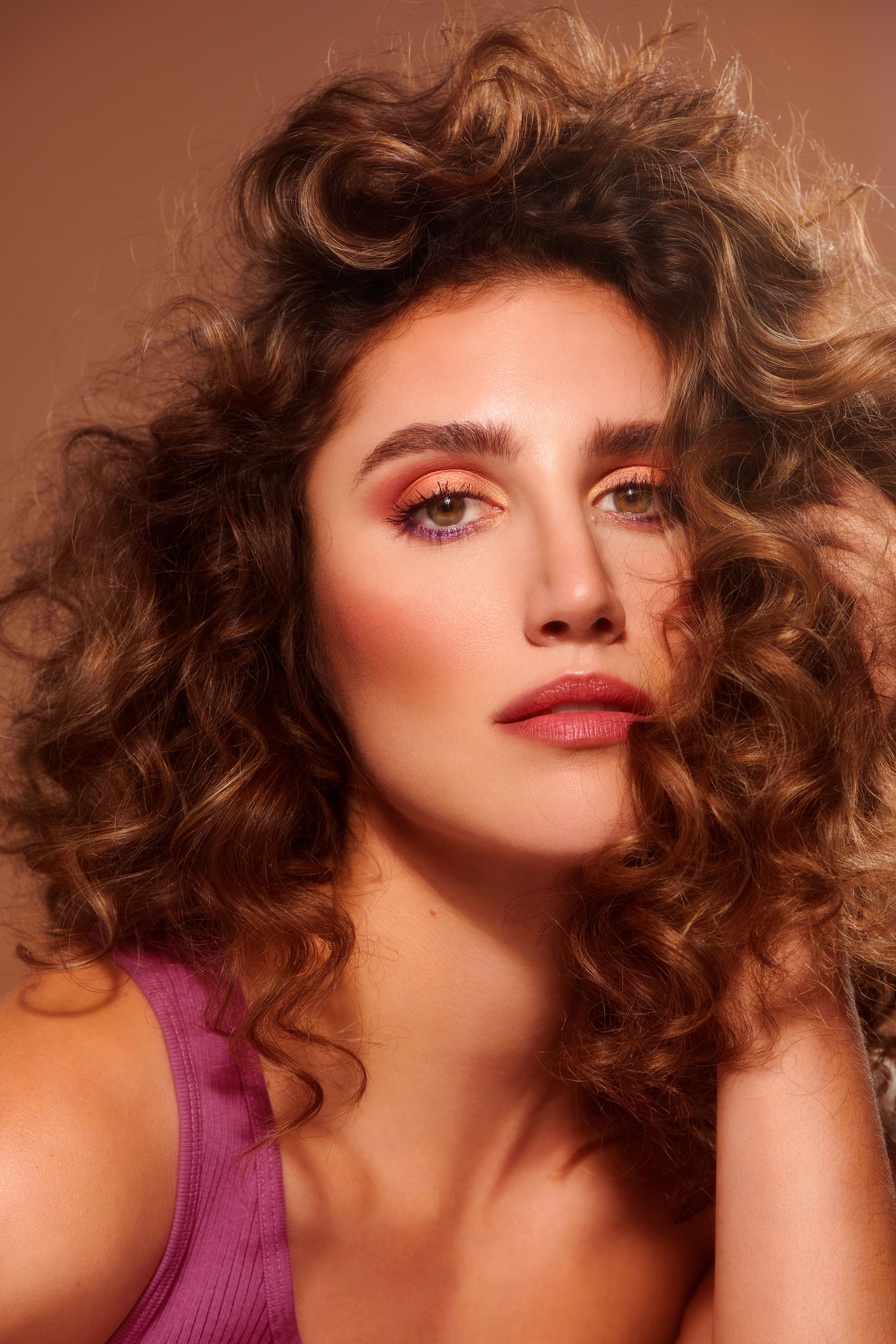Portrait of female model with high volume curls and warm-toned makeup wearing a purple tank top