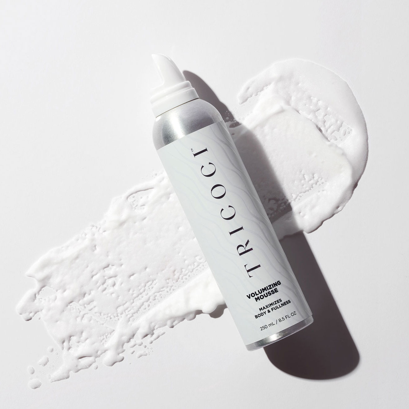 Bottle of volumizing mousse laying on sample of product