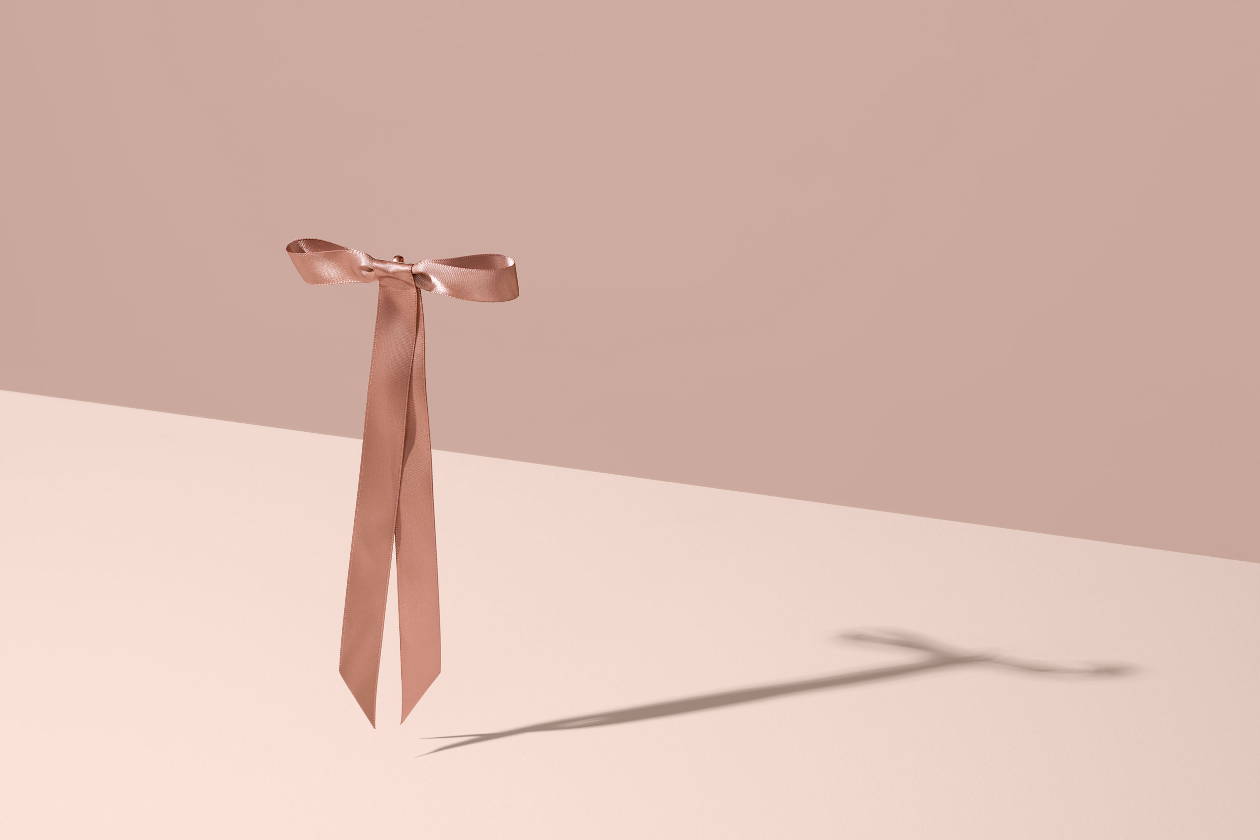 Ribbon tied in dainty bow suspended in mid-air with shadow