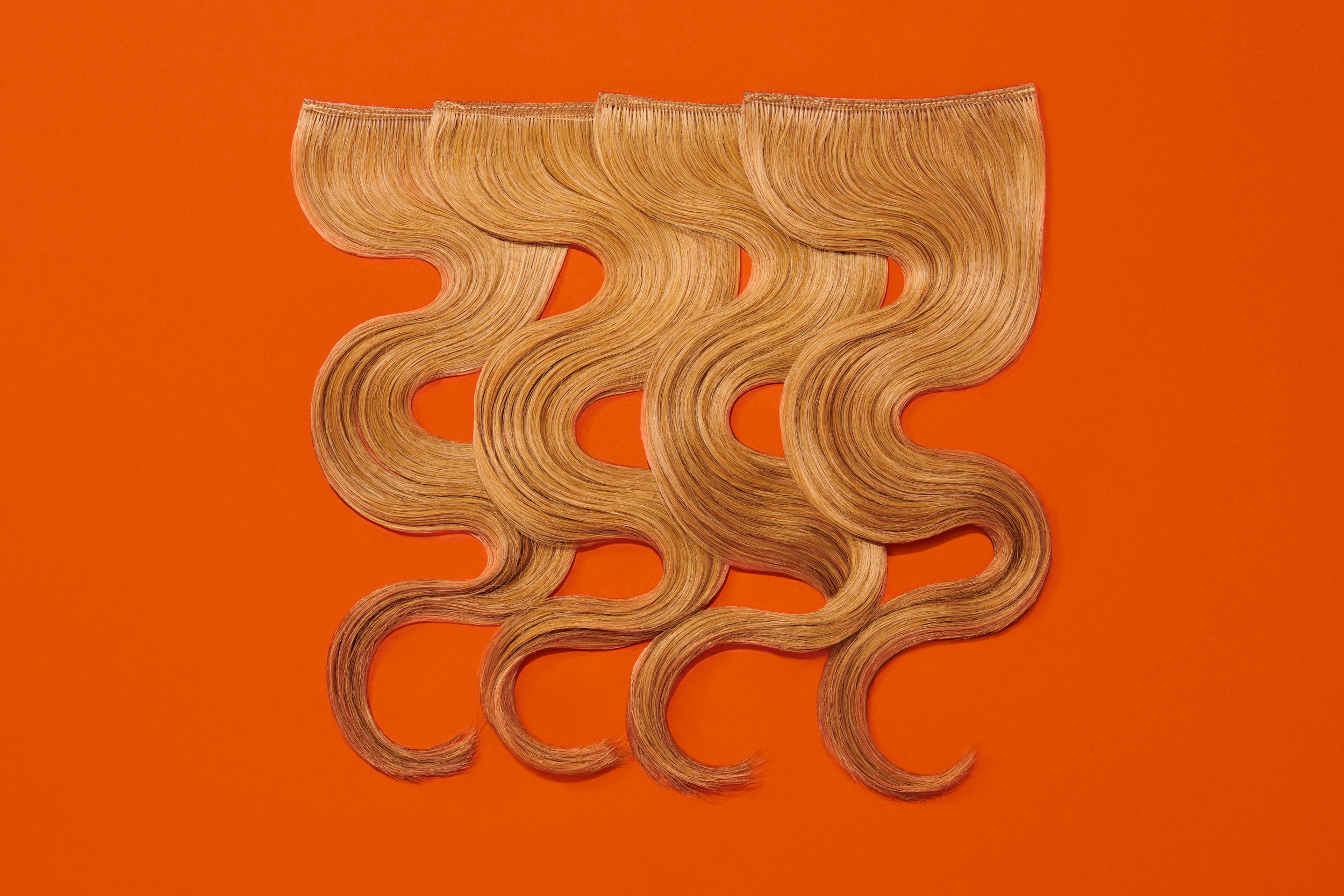 Caramel brown balayage-style hair extension wefts on orange background