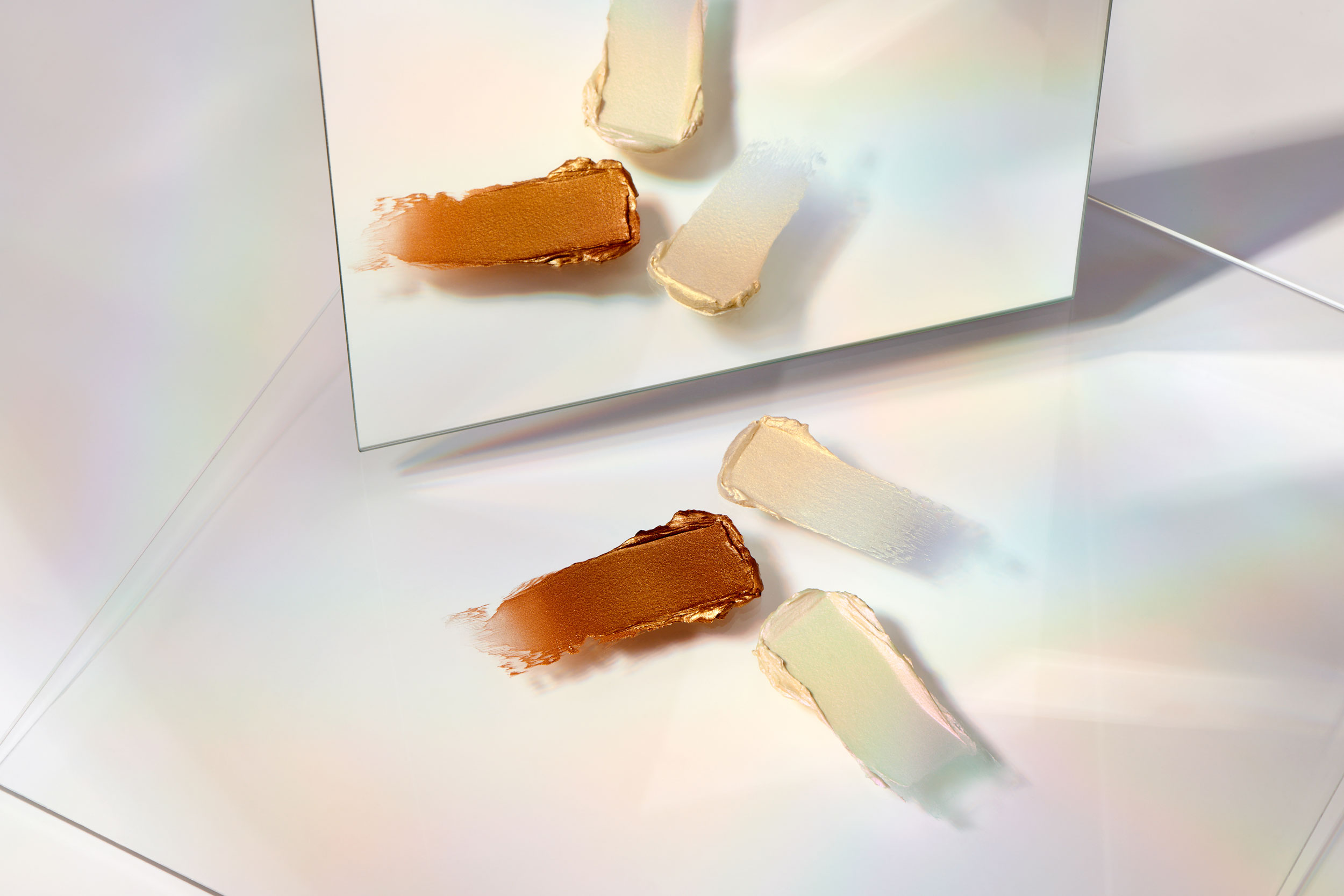 Three makeup swatches on clear surface with mirror reflection