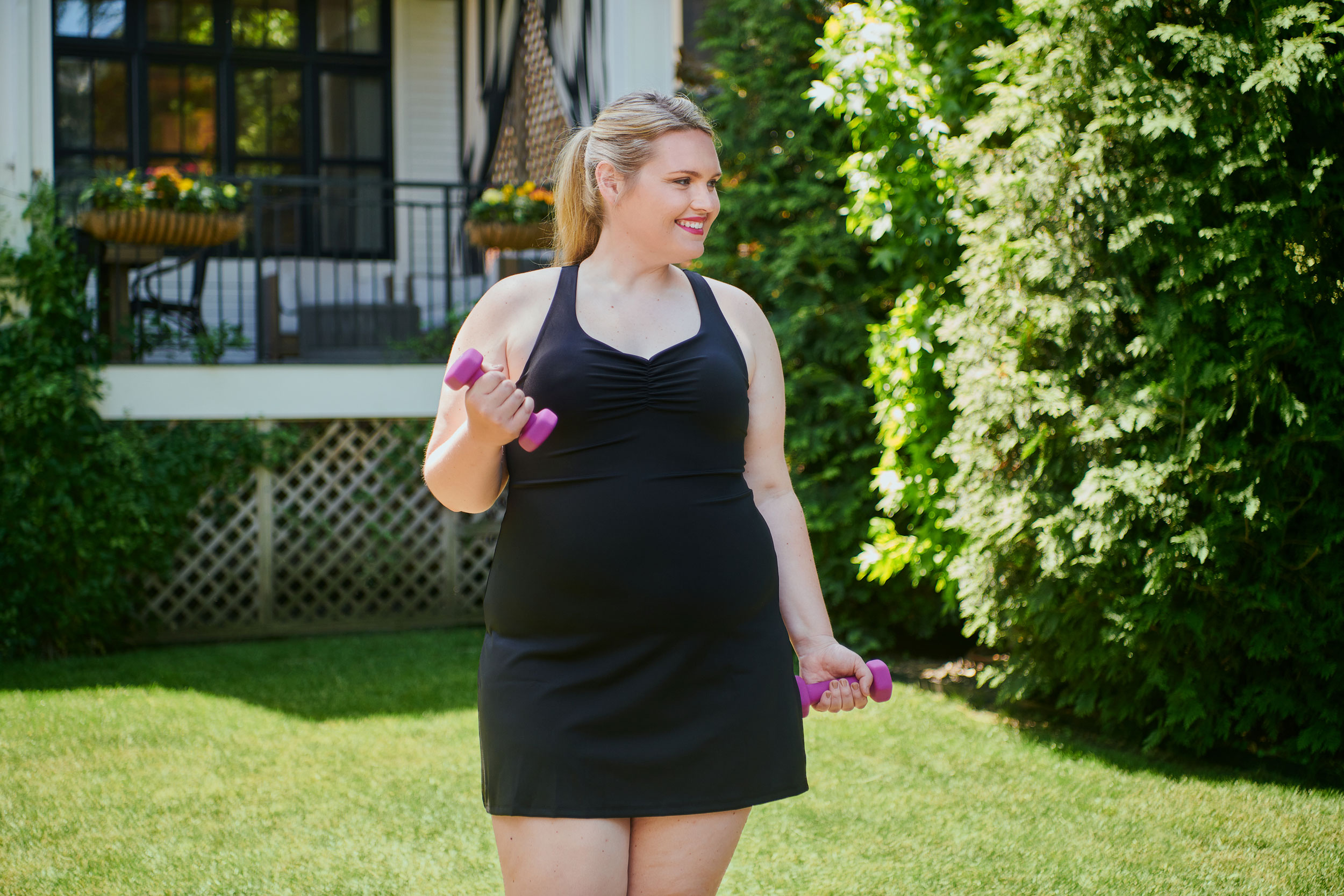 Plus-sized woman outside in black athleisure dress holding hand weights
