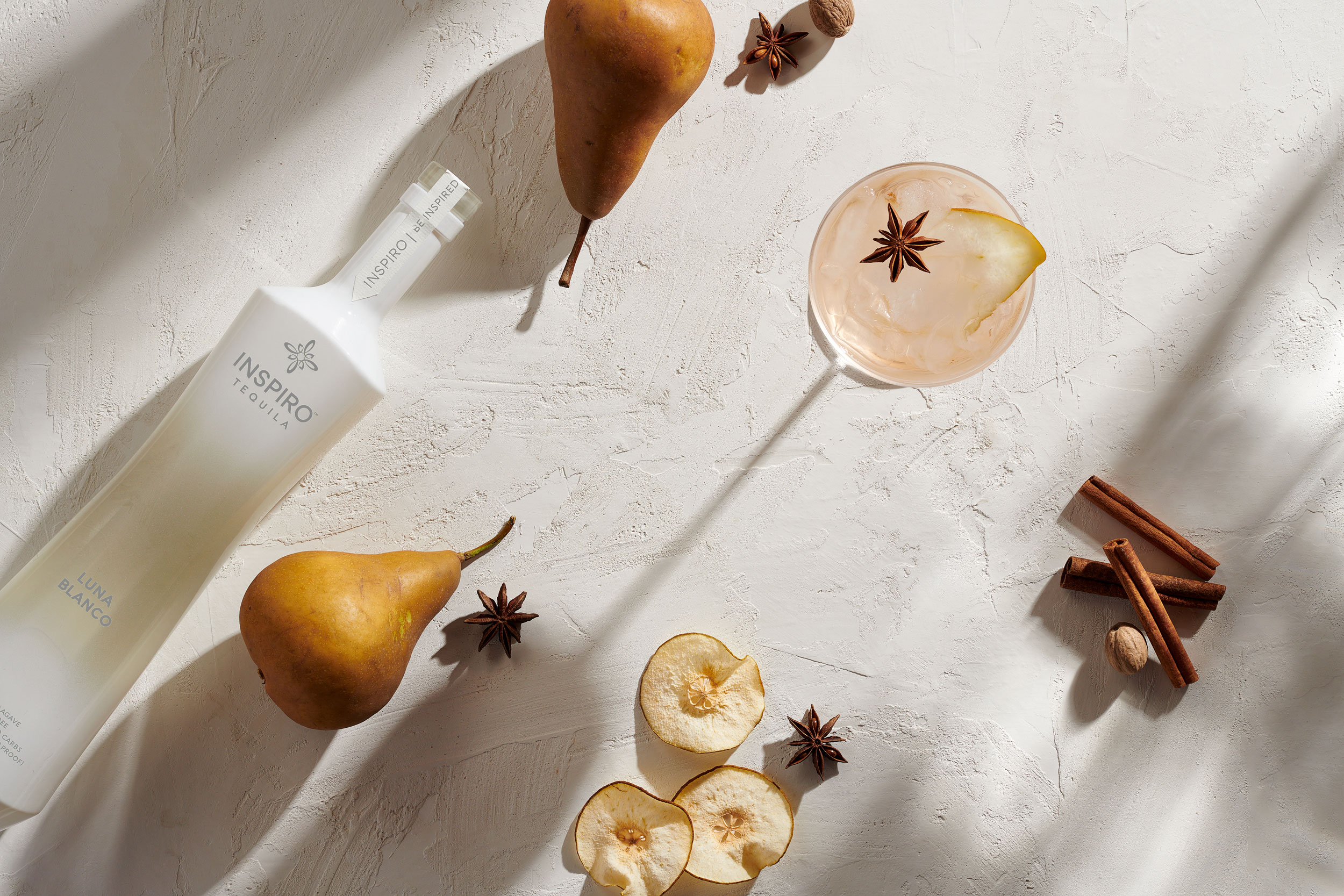 Overhead image of tequila cocktail, alcohol bottle, pears and spices