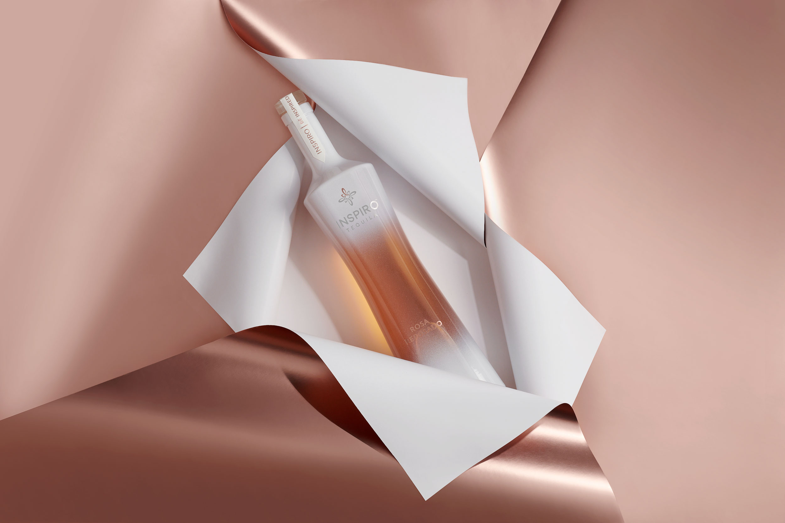 Bottle of tequila resting in the folds of rose gold paper